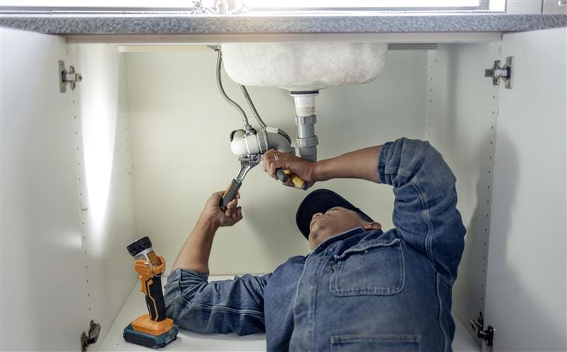 Plumber repairing pipes beneath a bathroom sink in Panama City