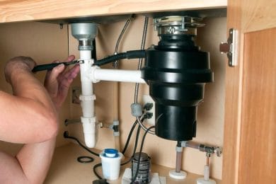 Plumber repairing a garbage disposal beneath a kitchen sink in Panama City