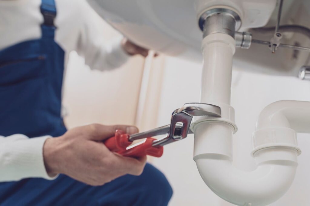 Plumber repairing a white drain pipe beneath a sink in Panama City